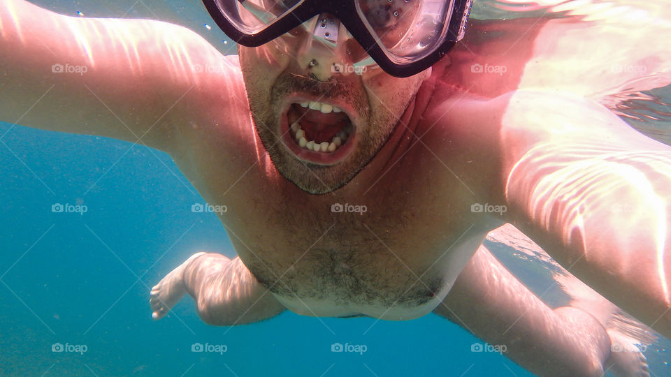 Man diving in the ocean, male underwater smiling,swimming and relaxing in big blue sea with his waterproof camera