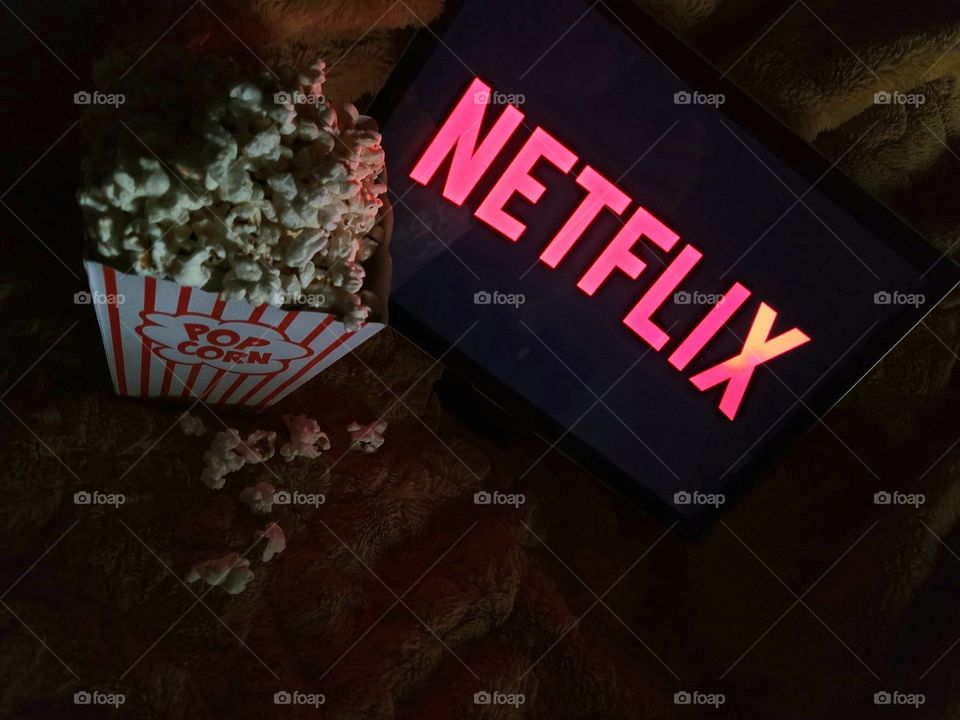 Laptop computer screen ready to watch Netflix for a fun, cozy, and relaxing night with popcorn as a snack, on soft bed blanket in dark room