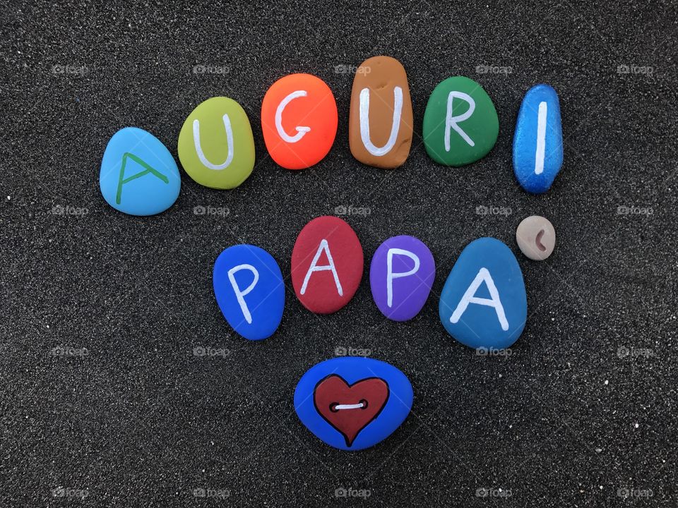 Auguri papà, father's day celebration in italian language with multicolored stones over black sand 