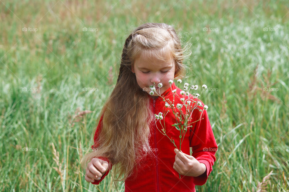 Little girl on the field on the countryside enjoying flowers and walking