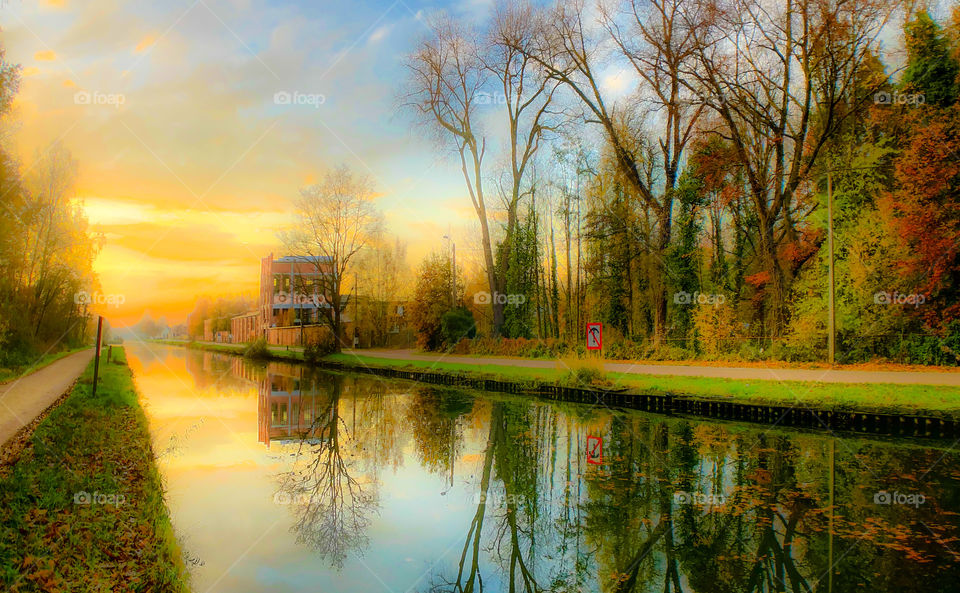 Dreamy fall landscape of a colorful sunrise or sunset sky reflected in the water of the river or canal