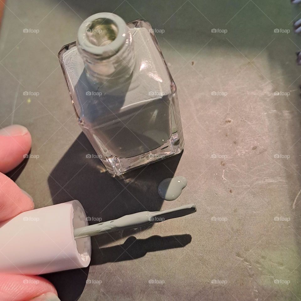 ladies fingers holding nail varnish brush and pot soft green painting, cosmetics