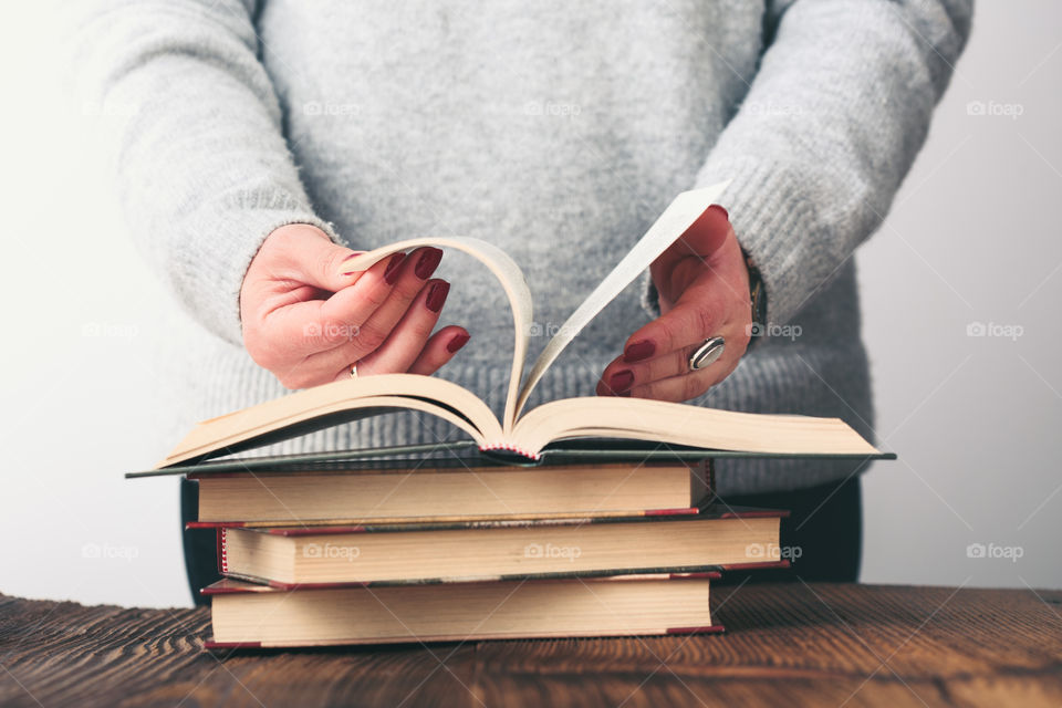 Young woman turning pages of old book on wooden table in antique bookstore. Woman wearing grey sweater and jeans. Vertical photo. Space for text