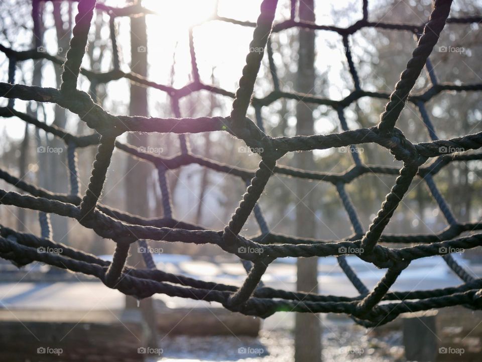 A web of rope on a children’s playground, with the sun and trees in the background. 