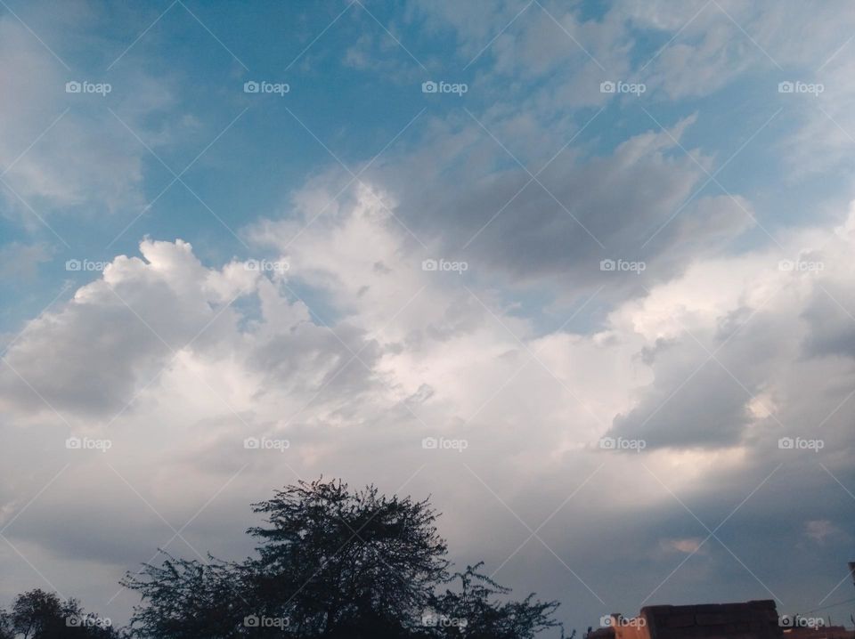 a shiney day white clouds in blue sky whitish cloud scattered dark tree looks very beautiful