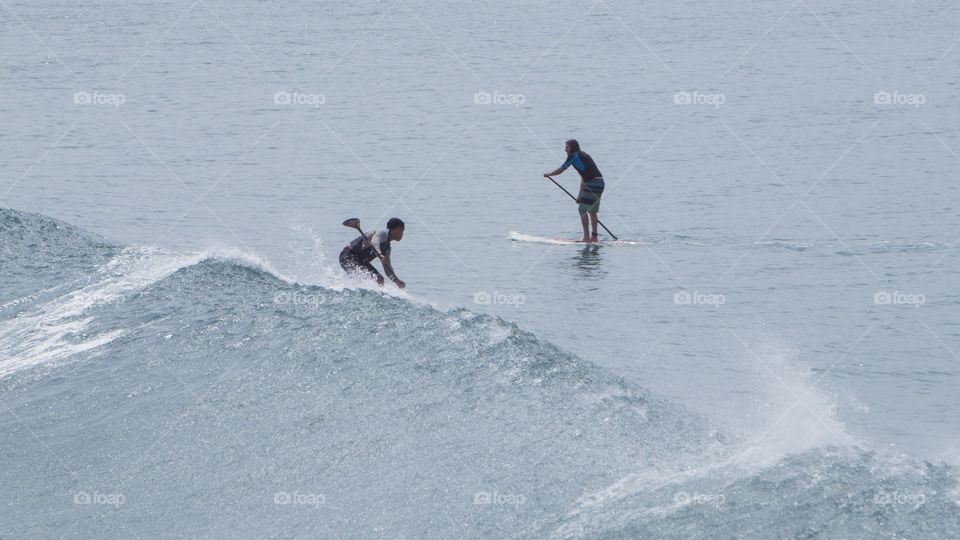 Two men surfing and paddling in the ocean during big waves