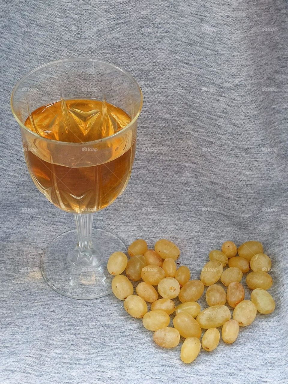 Wine glass with pale yellow wine and yellow grapes in the shape of a heart on a gray background