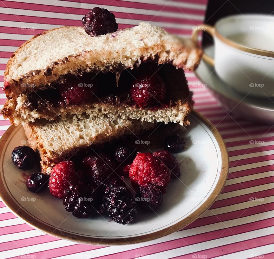 A yummy and delicious peanut butter and raspberry and blackberry sandwich on a white and pink striped background displayed with a tea cup for lunch. The USA, America
