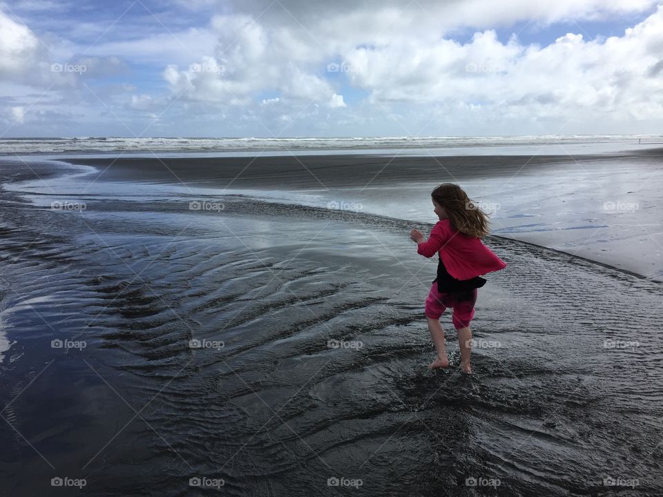 Playful science with girl tuning along the beach. Beautiful black sand beach, rugged nature. 