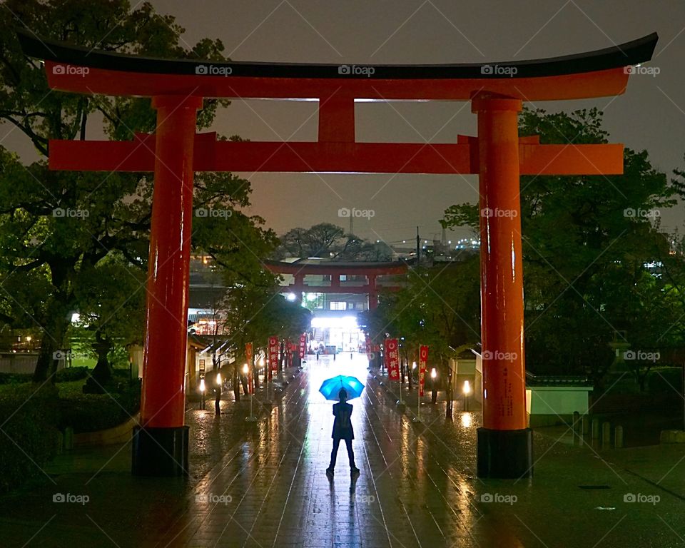 Main entrance to the Fushimi Inari Shrine on. Wet dark night with umbrella carrying man highlighted. Kyoto prefecture, Japan.