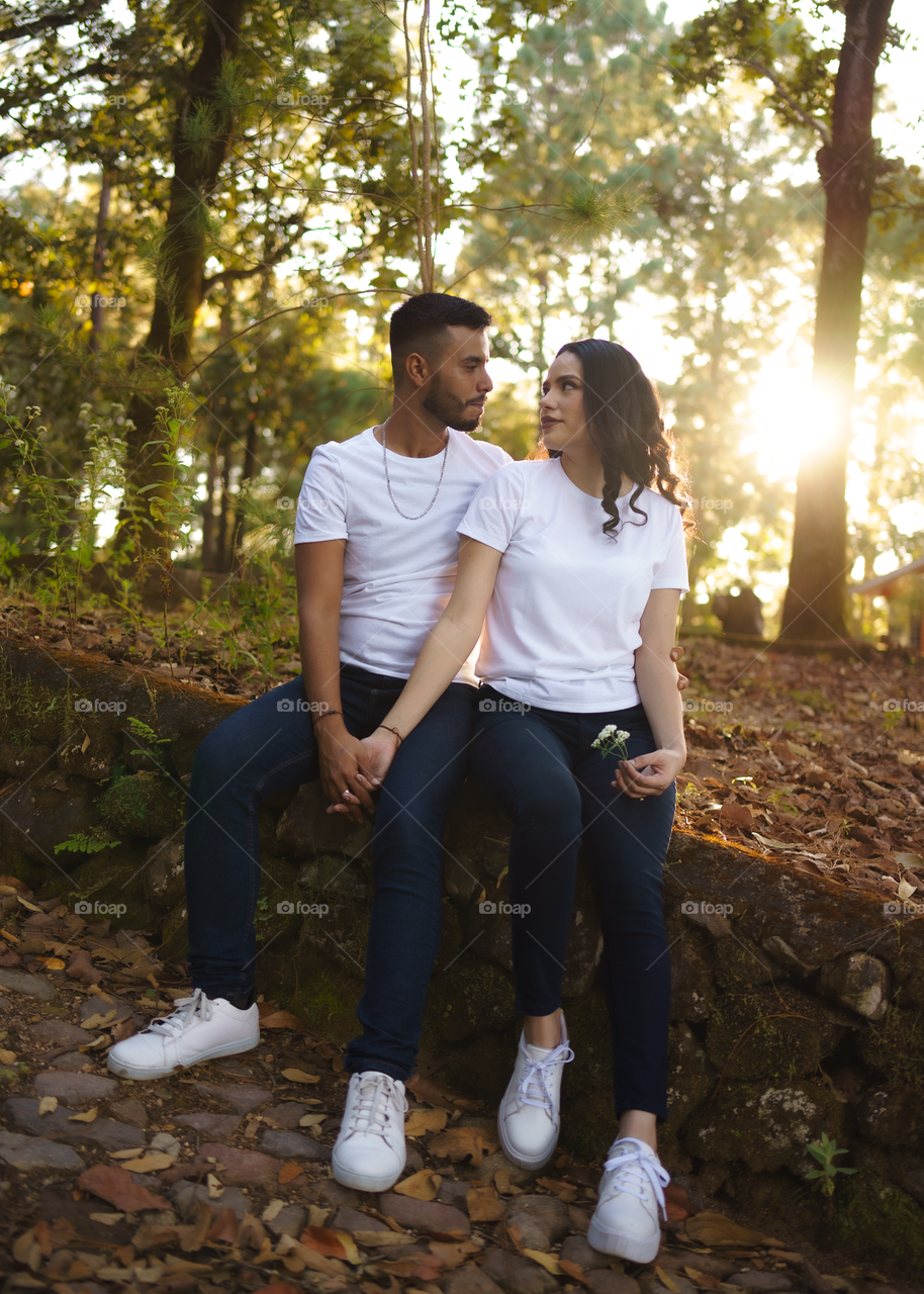 Couples of young people sitting in middle of the forest while looking into their eyes, in a sunny day.