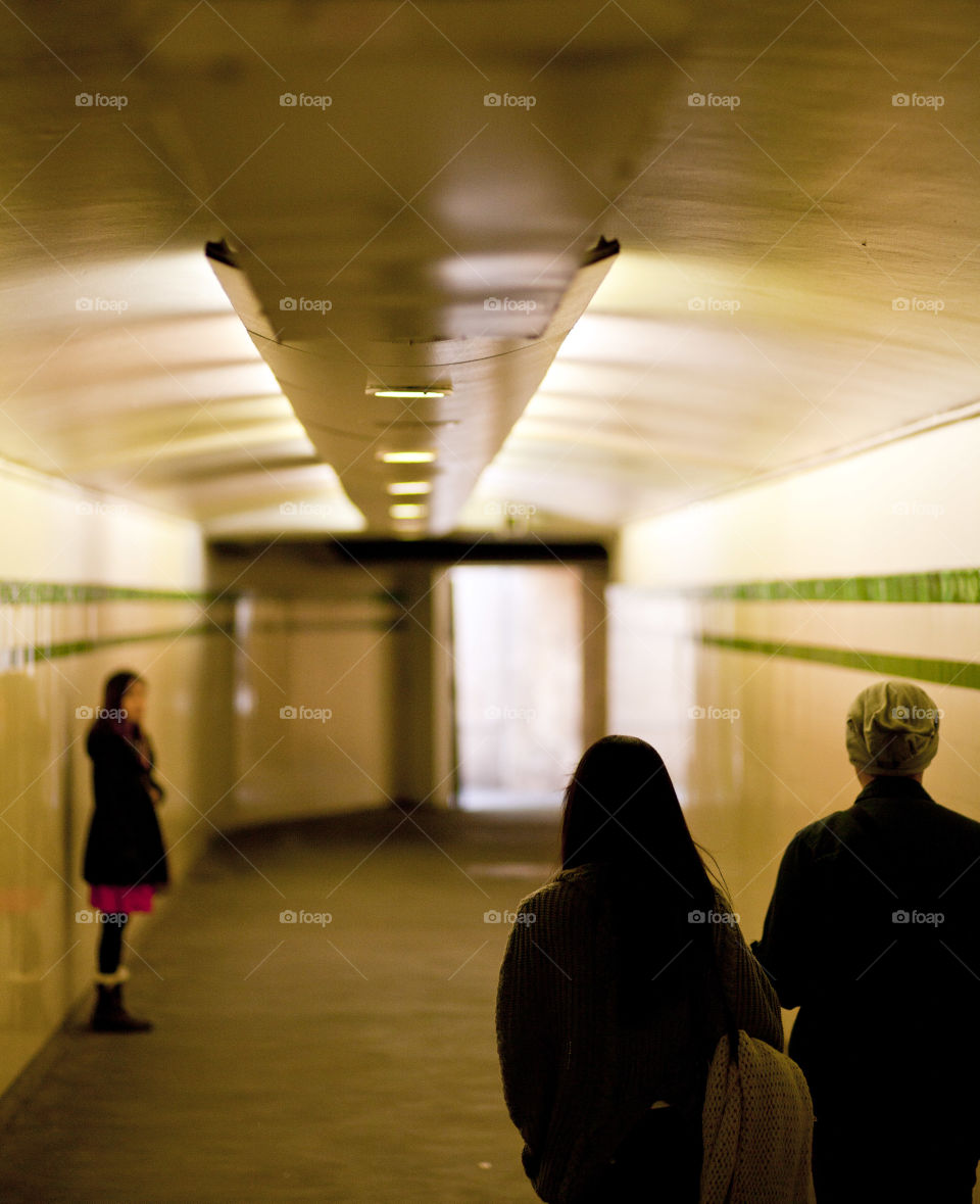 photo story, a girl waiting standing and two people walking in a tunnel