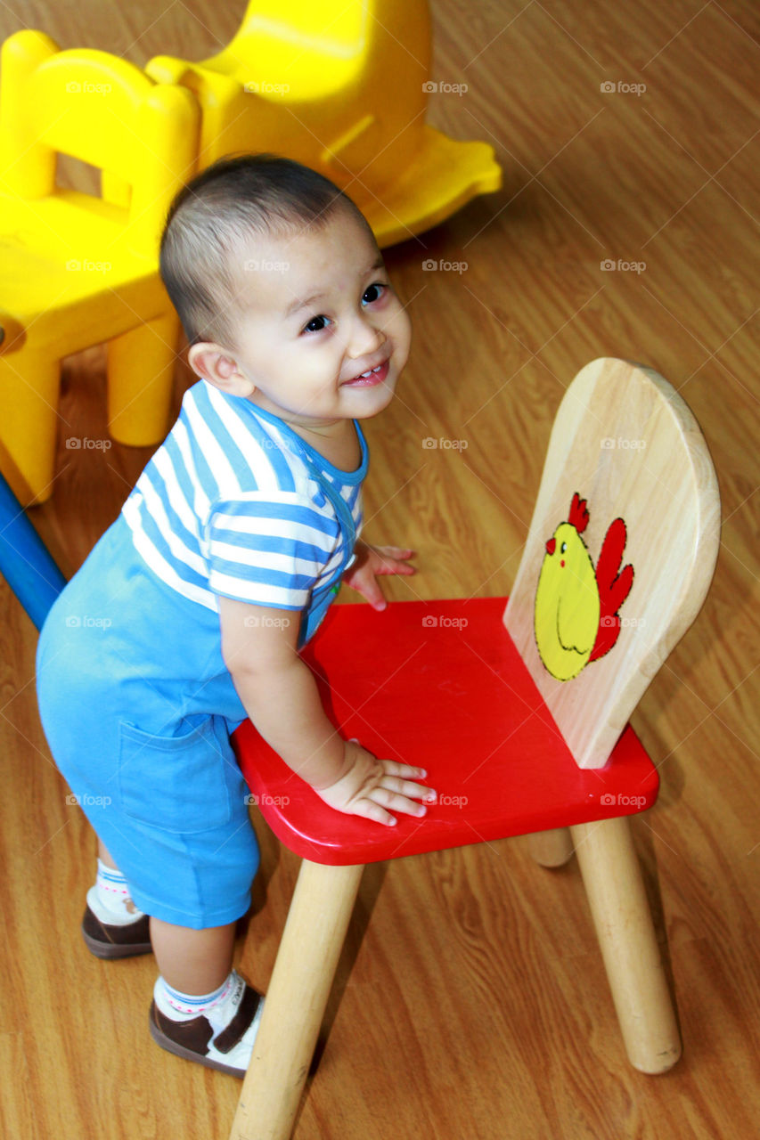 young smiling boy taking a wooden chair 