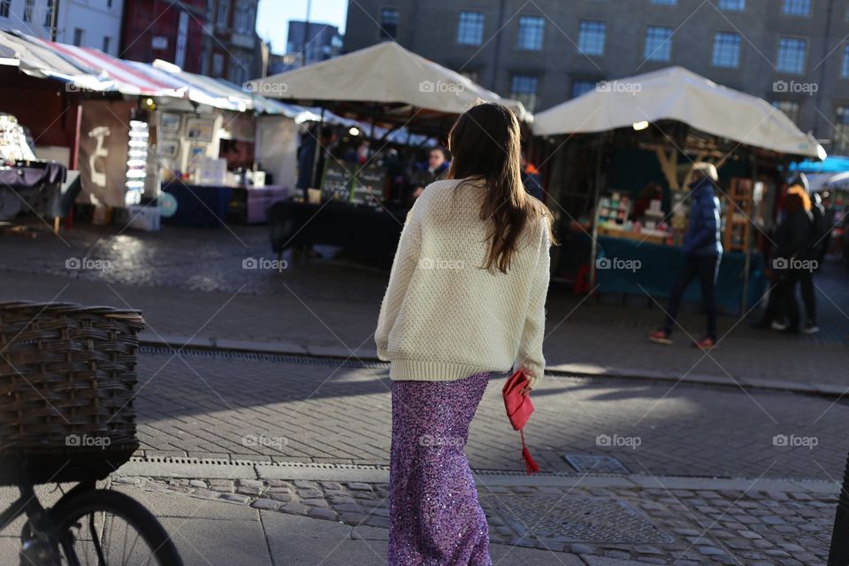 stylish young woman with a long brunette hair wearing long sequin pink skirt walking gracefully in the market