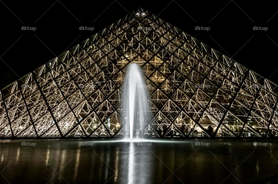 A lit up fountain outside the Pyramide du Louvre in Paris at night