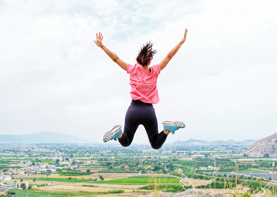 Young active girl jumping at the top of a mountain