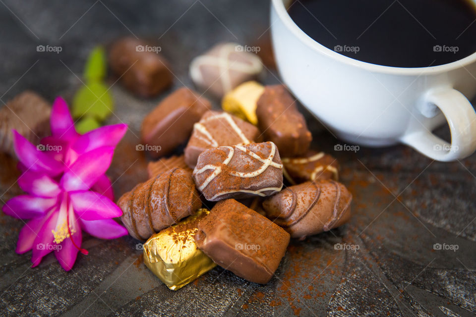 Close up of sweet milk chocolate pink flower and a cup of coffee on a dark background