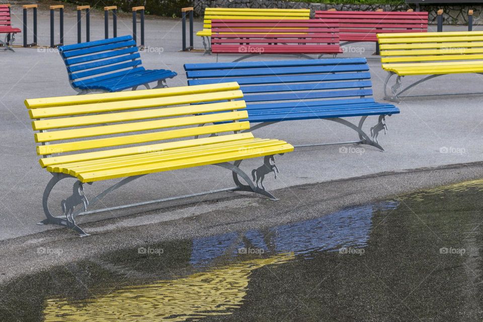 Several colourful yellow, blue and red benches near the puddle after the rain