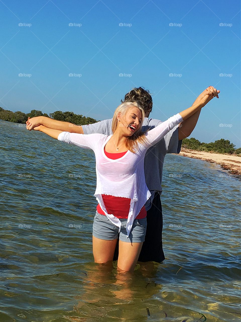 Couple standing back to back in sea and holding hand