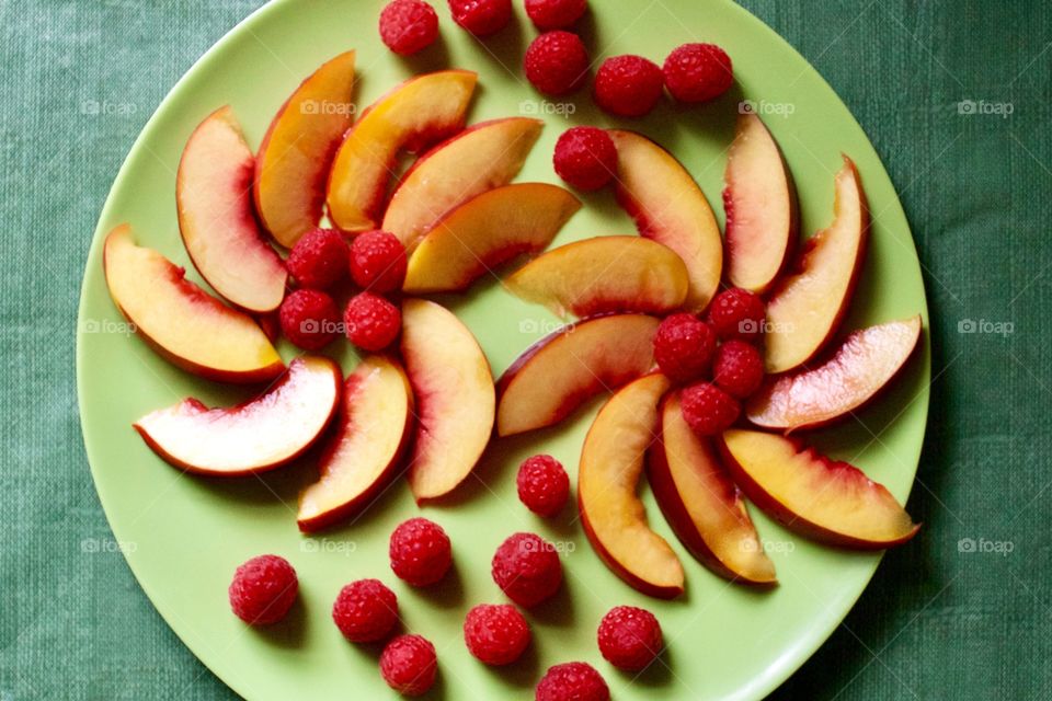 Flat lay of a decorative arrangement of fresh nectarine slices and raspberries on a green plate with green background 