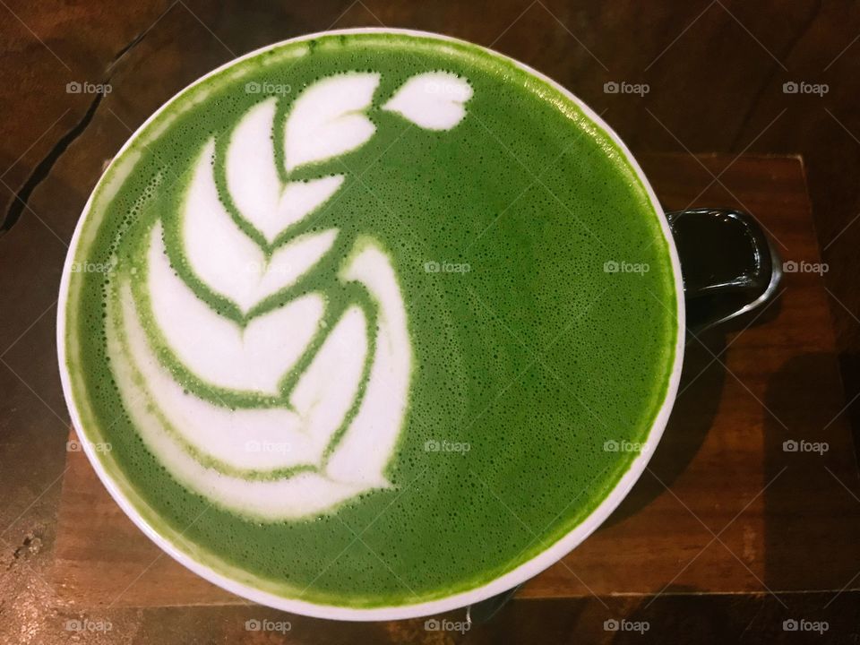 A Matcha cup have a very beautiful green color, above them forming a leaf by milk . I'm enjoying my matcha latte, resting time, 