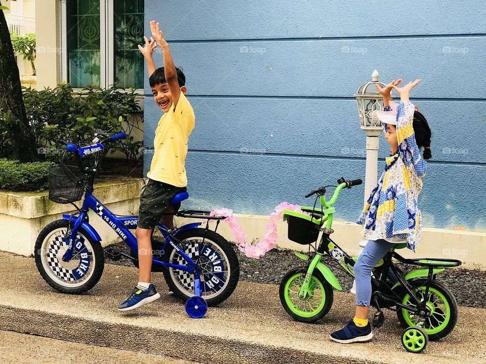 A boy and girl cycling and enjoying and a flower garland connected between two cycles to pull 