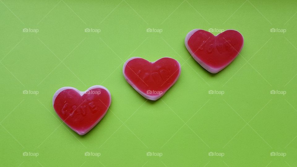 Three red candy hearts on bright green background 