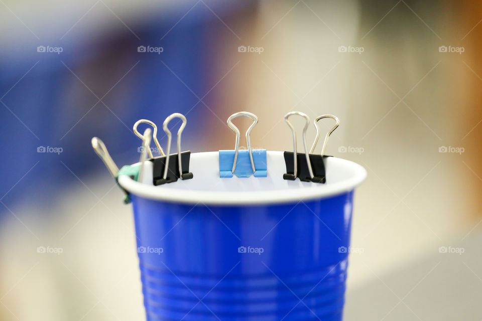 Colorful small binder clips attached to a blue drinking cup in an office 