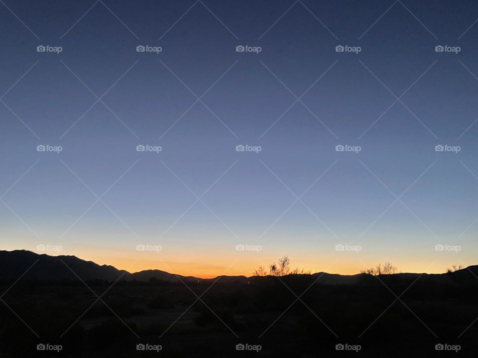 A orange and yellow sunset with mountains and tree branches 