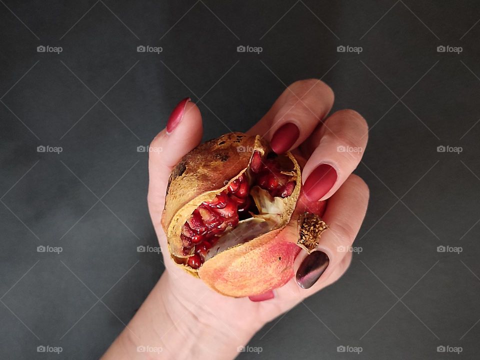 Beautiful female hand with nice art manicure holding a ripe pomegranate