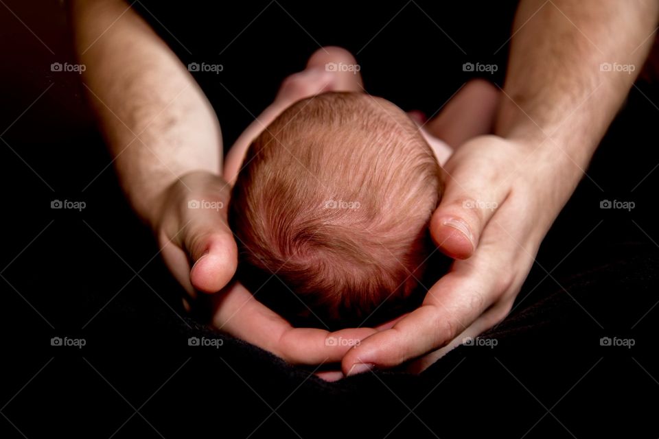 Baby boys head in dads hands