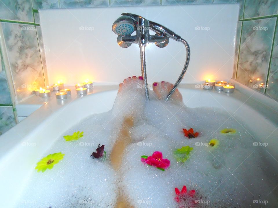 Woman's feet with red nail polish in bubble bath with candles and flowers