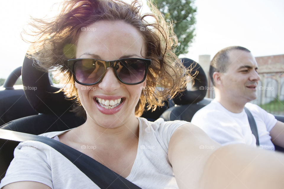 woman and man in convertible. woman smiling while driving in convertible auto with sunset behind her and wind blowing her hair