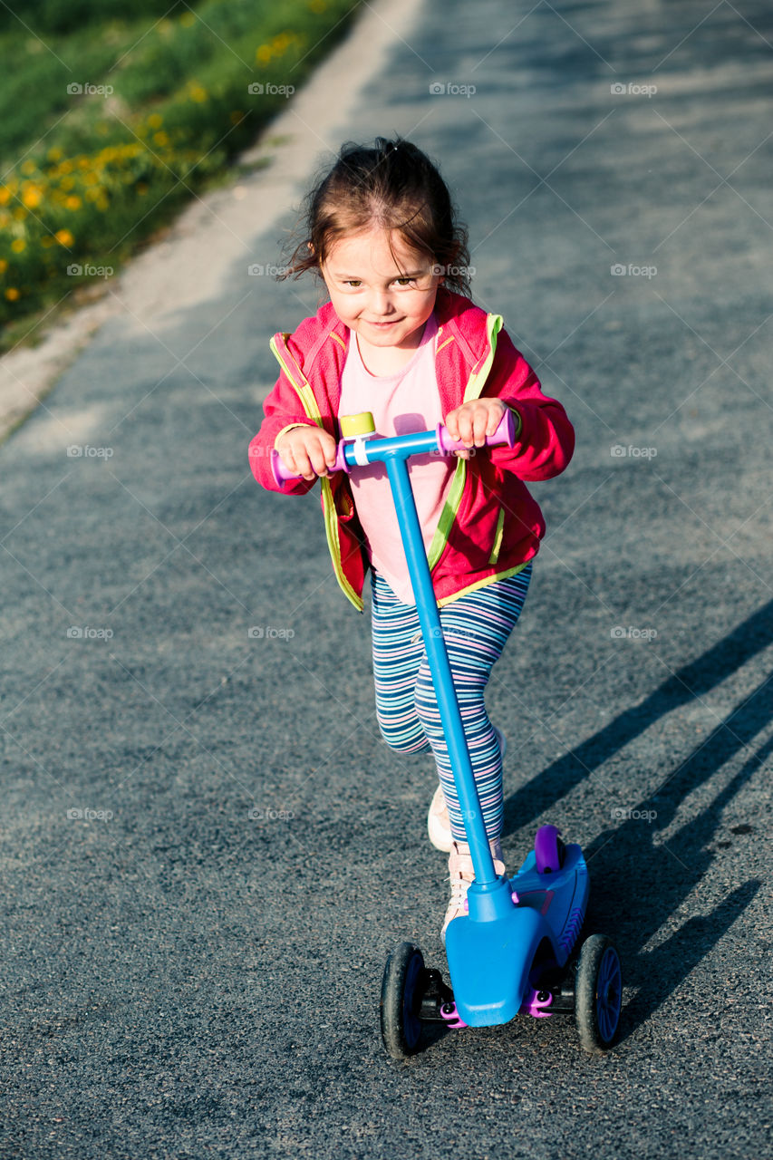 Little adorable girl having fun riding on scooter, playing outdoors. Real people, authentic situations