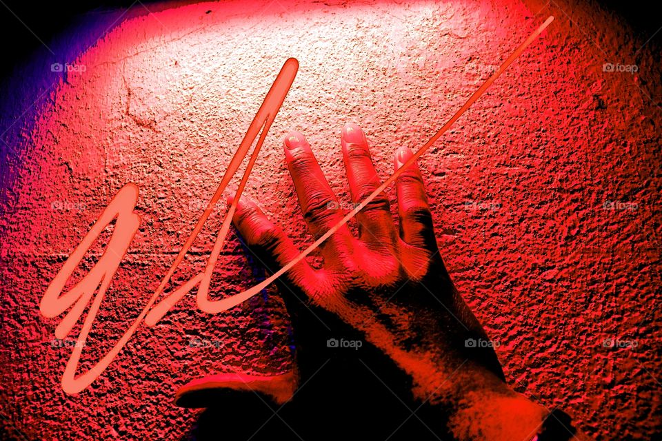 A man places his hand against a stone wall lit with neon red lighting and scribe is written on it.