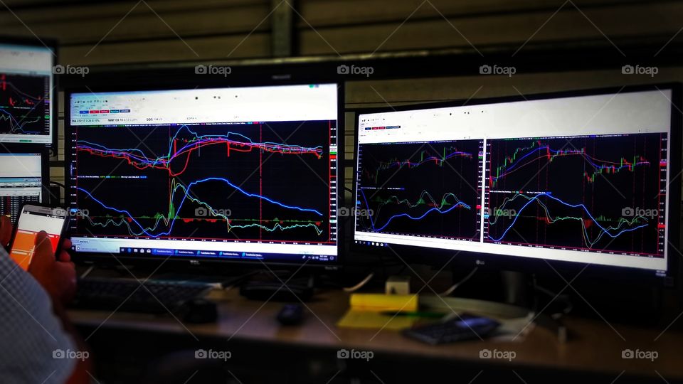 A man sitting at his desk holding his cell phone watching stock market charts on three computer monitors favorite gadgets