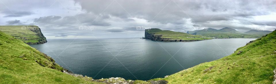 Cloudy sky reflected in grey sea with green cliffs in the Faroe Islands 