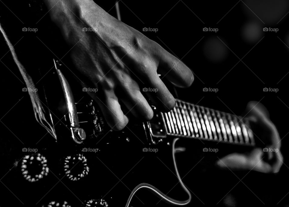 A musician’s hands play his guitar in black and white