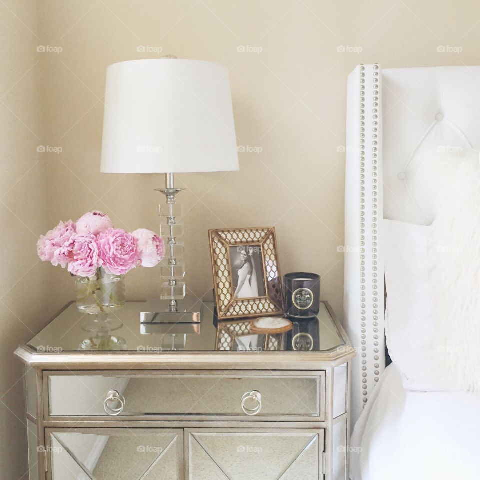 Bedside Scene. Glamorous mirrored nightstand next to a white tufted bed