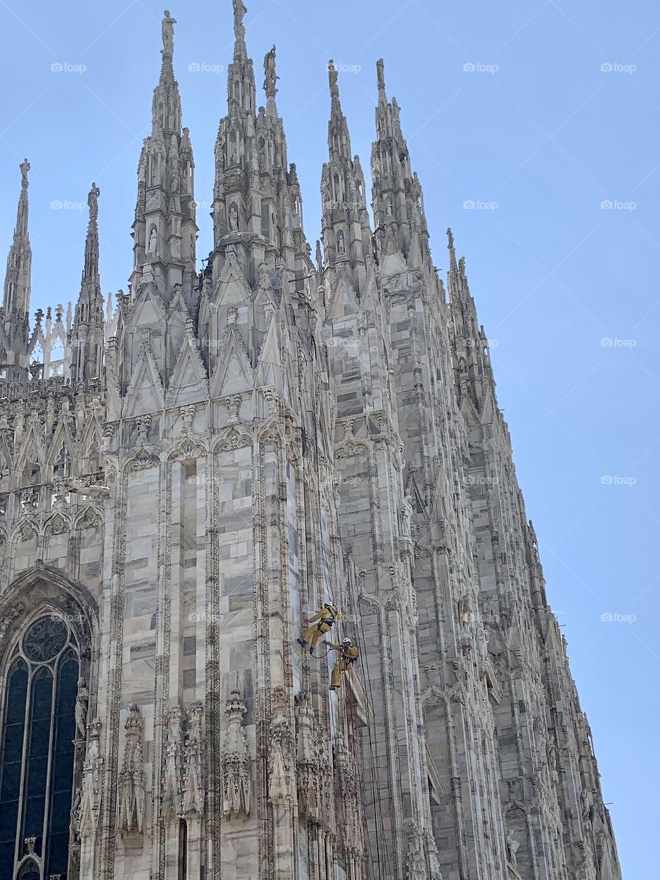 Two people climbing Duomo church to clean it . 