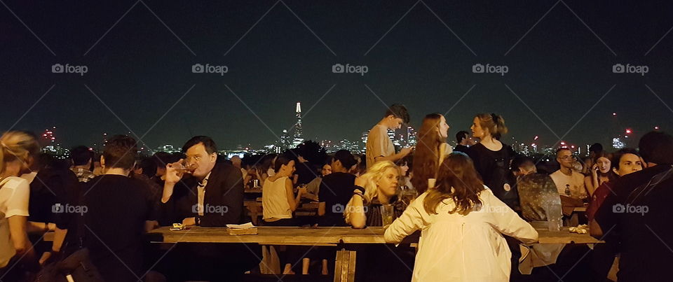 A busy rooftop bar with city skyline background.