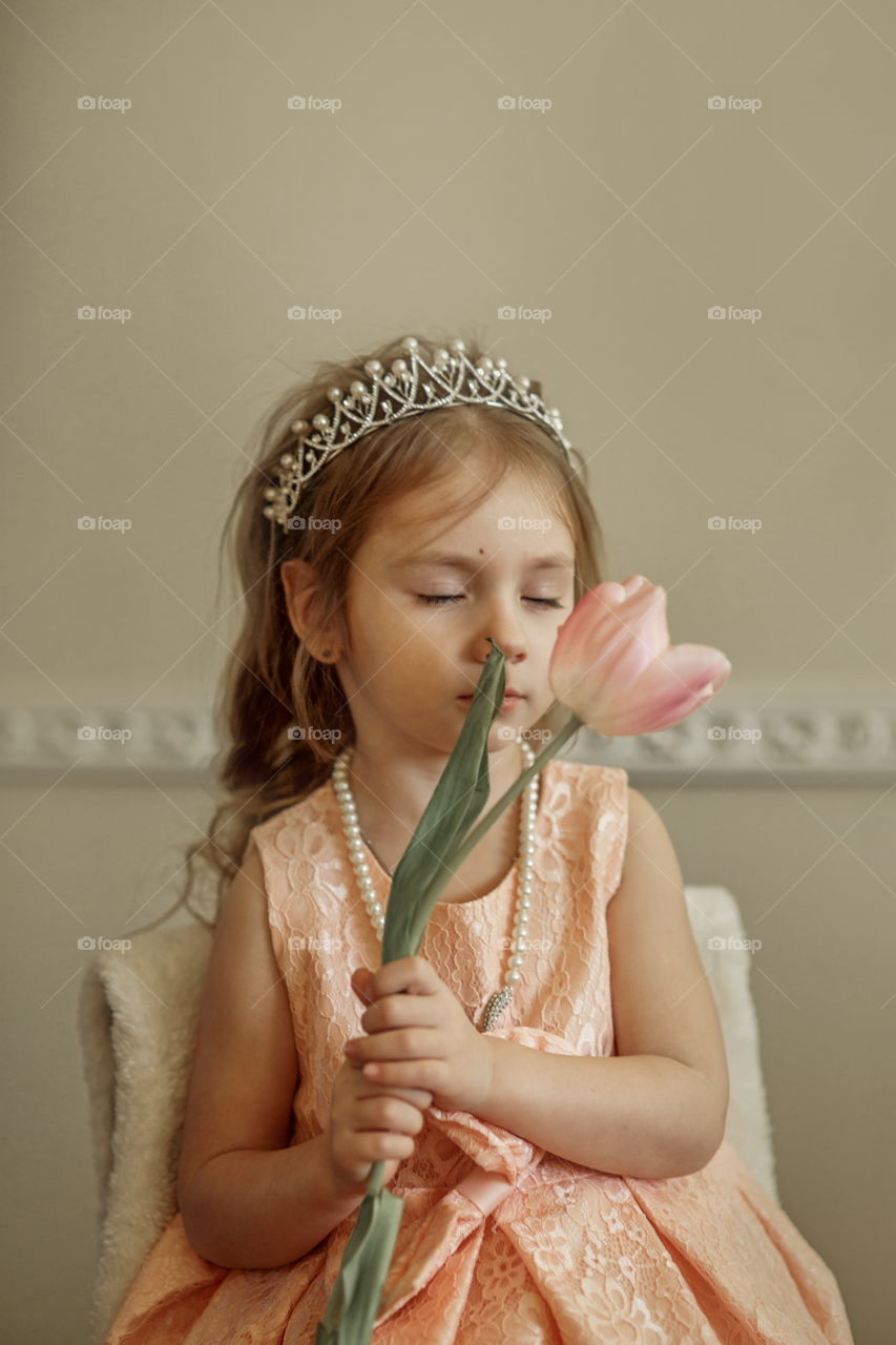 Vintage portrait of a beautiful little girl in pearl crown with tulip flower