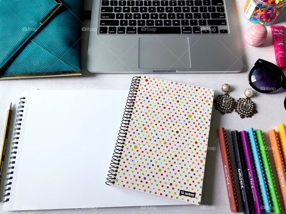 Top view of women's work desk with stationary, laptop, notebook, fashion accessories and empty sketch book.