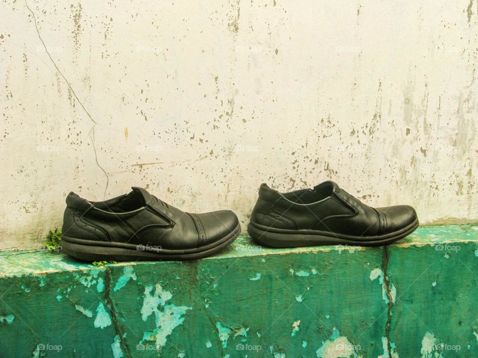 Close-up of a pair of black shoes resting on the edge of an old, peeling concrete wall in high angle view