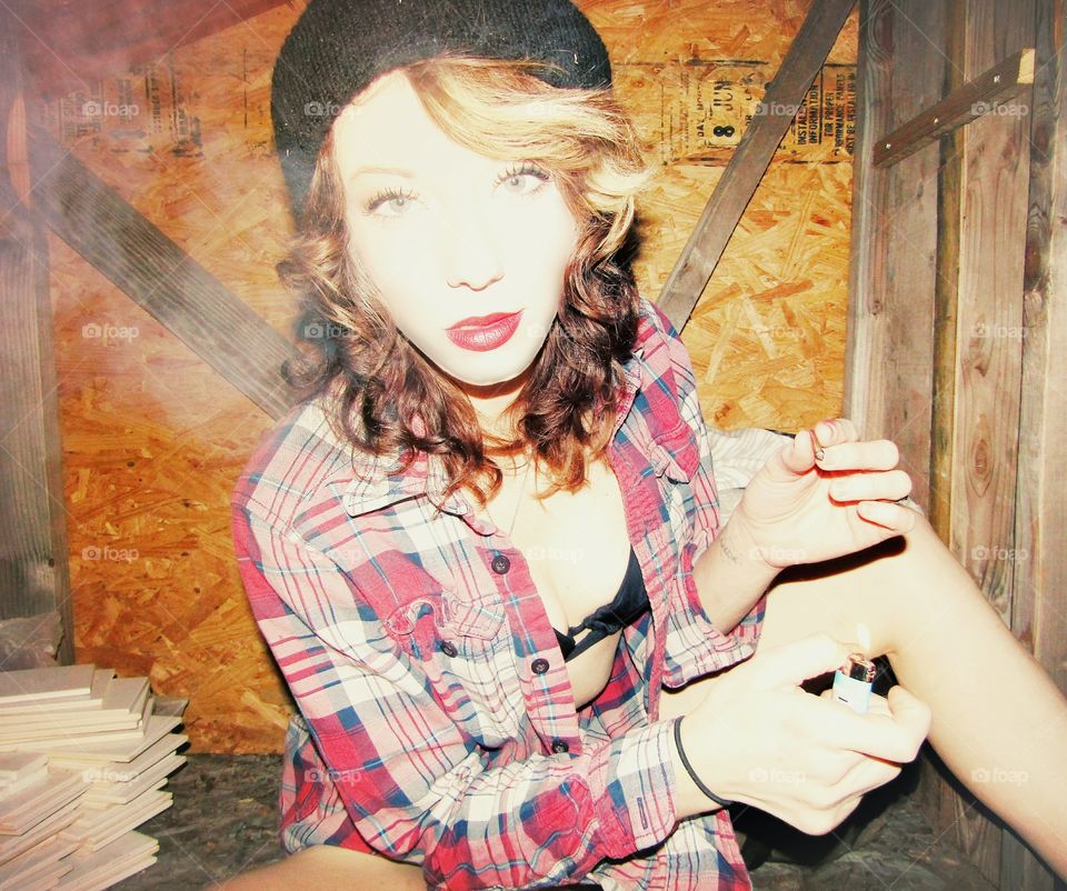 young adult white female or stoner chick (gray eyes red lips) in revealing clothes with a plaid flannel, a beanie surrounding golden brown blond curls, with red lips smoking the end of a marijuana blunt while holding a lit Bic lighter.