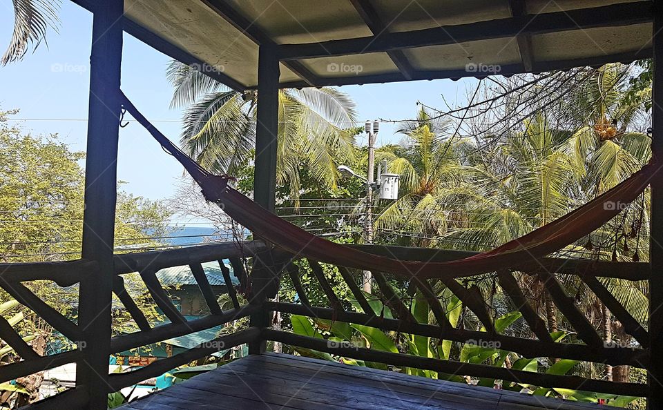 Hammock hanging on the patio of a house with an ocean view in Montezuma Costa Rica with lush trees and the sea in the background. A relaxing spot with a view.