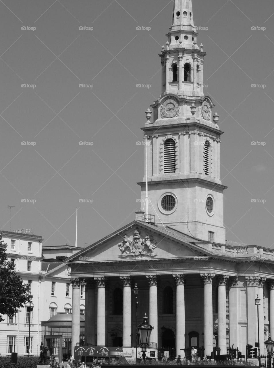 An old ornate building with a clock in its tower, many pillars, and decorative carvings on a sunny summer day in London. 