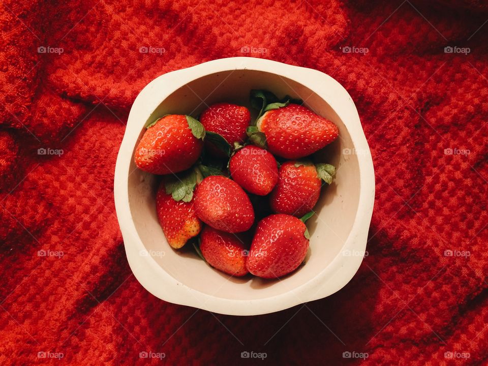 Strawberries in a bowl on red background.