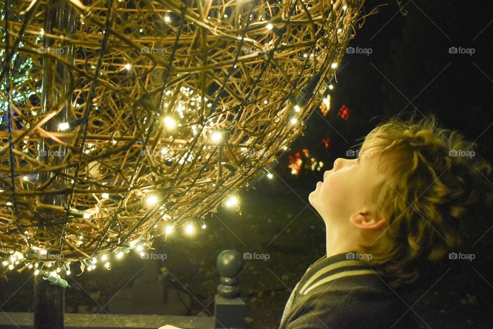 Side view of a young boy gazing up at a big ball of festive lights