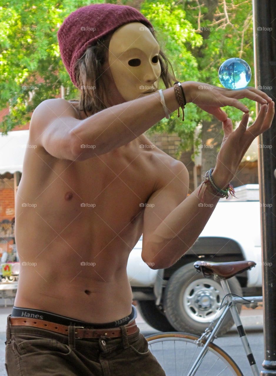 A masked street performer does amazing movements with a glass ball. 